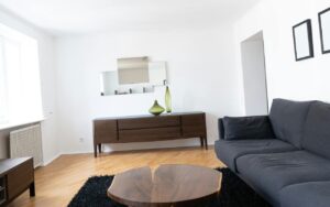 Dnevna soba sa braon stočićem, sofom na crnom tepihu i komodicom pored zida